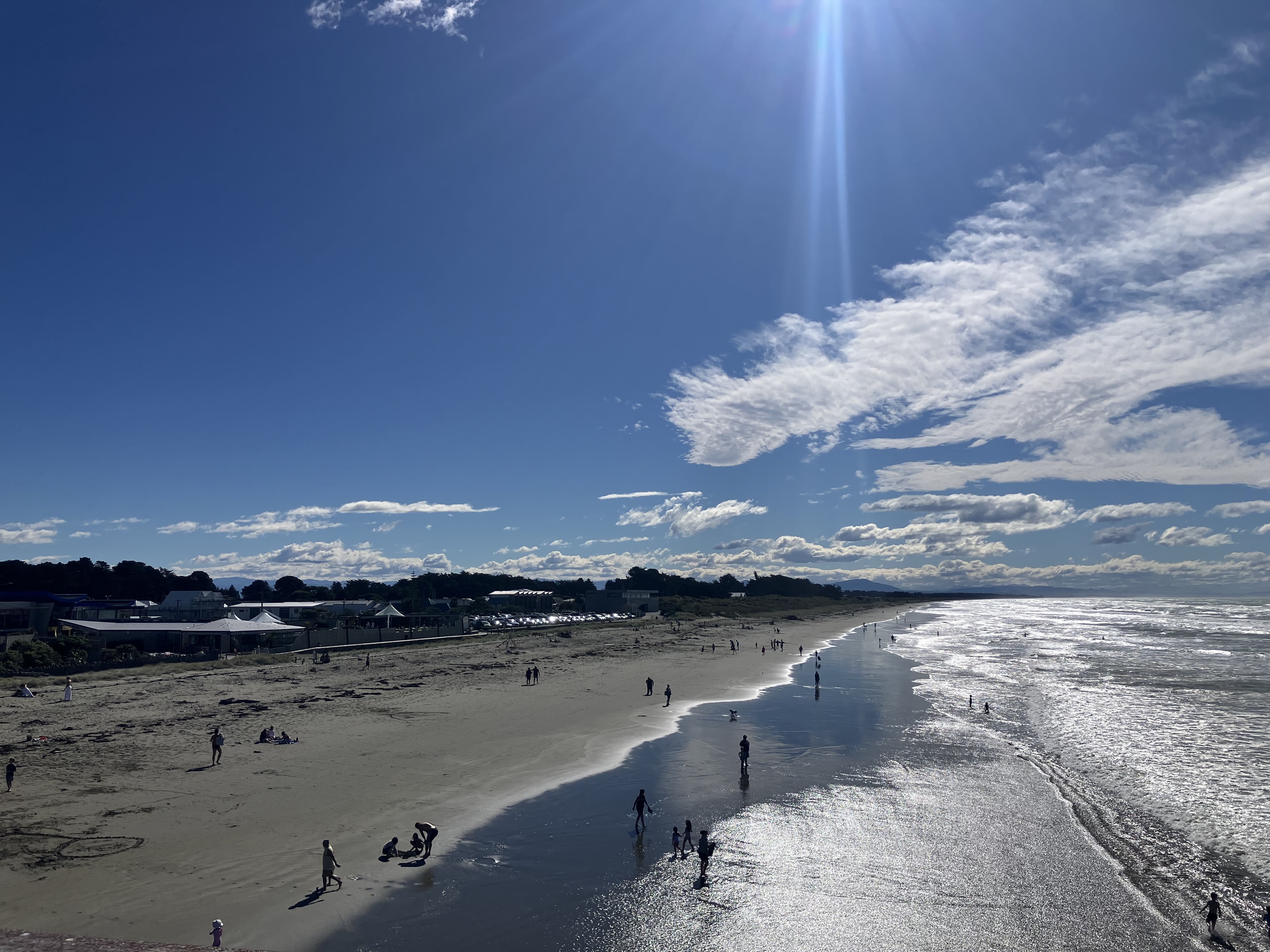 Photo taken on New Brighton pier, looking north along the beach to show people on the beach, community facilities and in the sea, to denote togetherness and variety. Copyright: aimee whitcroft, 2026.